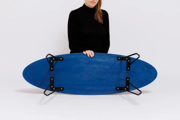 Na obrázku je Surf tolek, jeden z produktů značky REZ design, a figurantka ukazuje jeho modrou spodní část, která symbolizuje vlny moře.